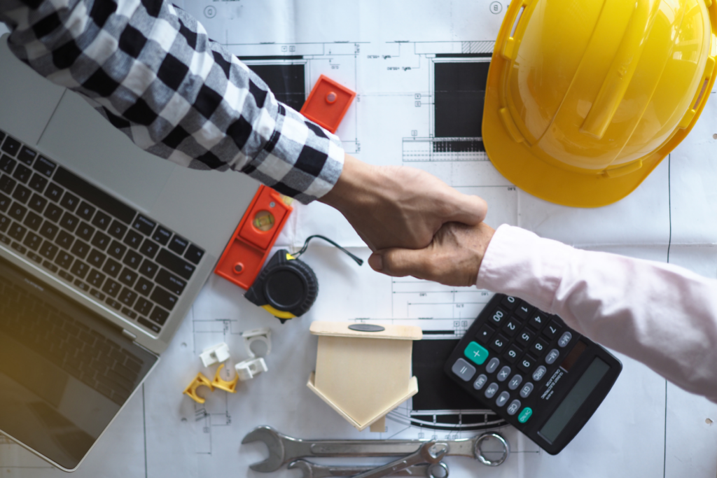 Contractors reviewing building plans with a laptop, calculator, tools, and hard hat