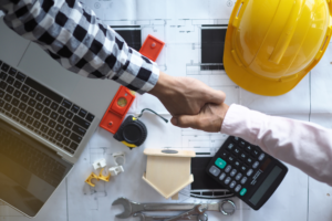 Contractors reviewing building plans with a laptop, calculator, tools, and hard hat